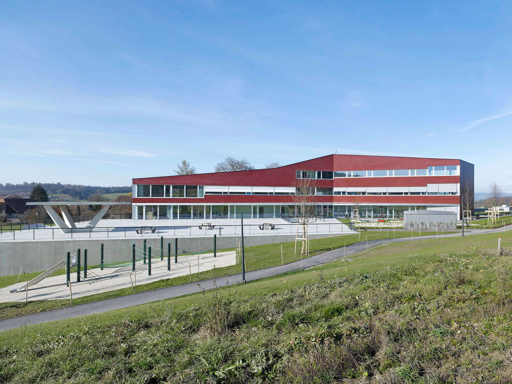 Der Pausenhof befindet sich auf einem Betonsockel, der dem nach Südwesten abfallenden Hang entwächst. Er beherbergt die Turnhalle sowie Umkleide-, Sanitär- und Geräteräume.