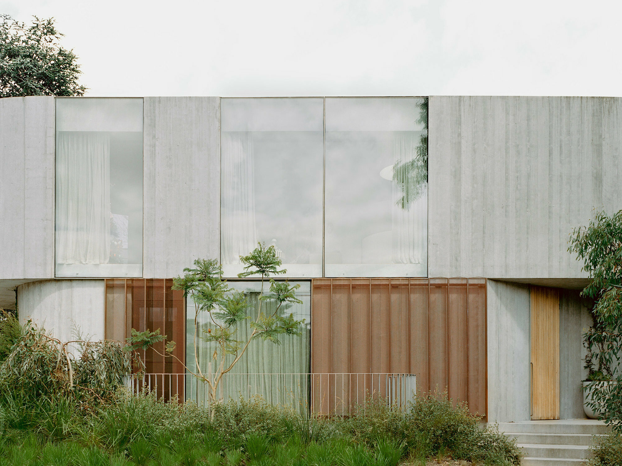 Die raue Struktur von Sichtbeton wechselt sich beim Wohnhausprojekt im australischen Kew mit weicher gezeichneten oder warmen Oberflächen an der Fassade ab.