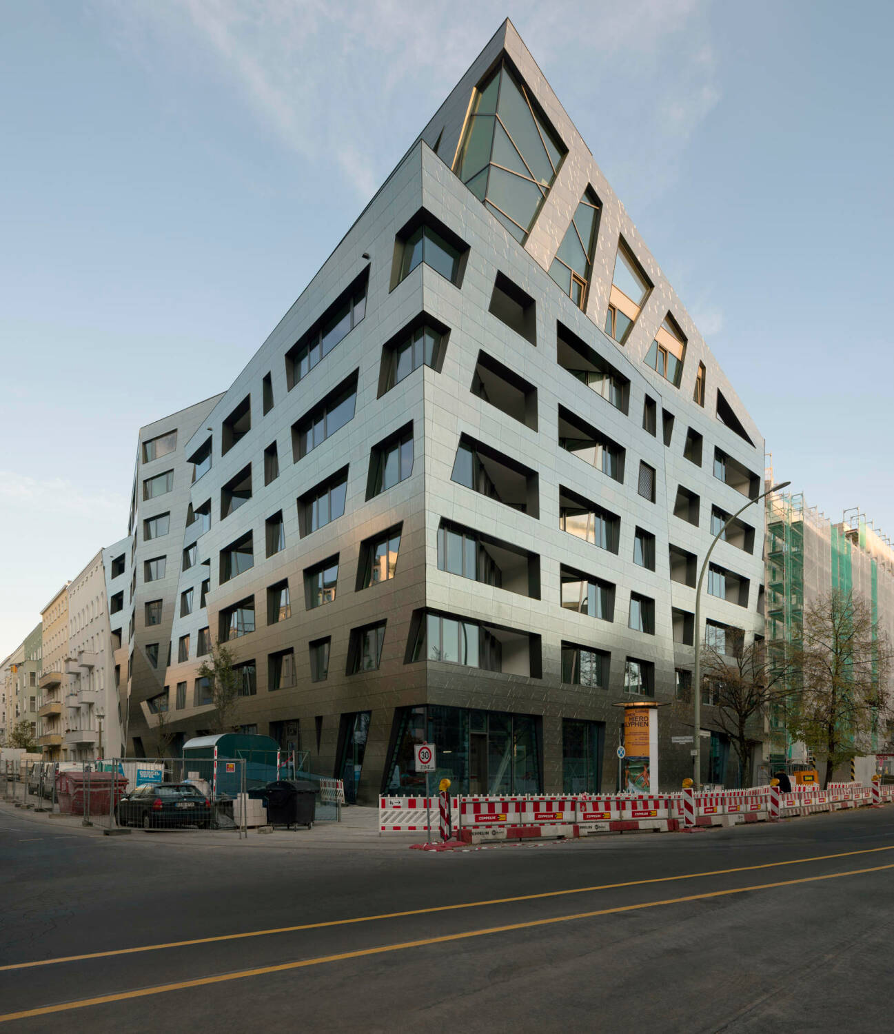 Die hinterlüftete Fassade der komplexen Gebäudegeometrie ist mit bläulich schimmernden Feinsteinzeugplatten verkleidet.