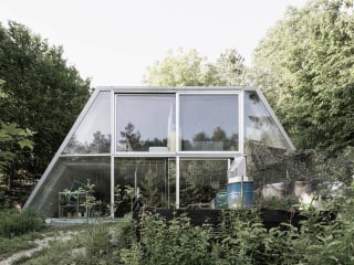 Das Haus ist als eine Art trapezoides Zelt konzipiert. Als selbsttragende Schale aus Beton schiebt es sich halb in einen nach Süden abfallenden Hang und verschmilzt durch ein Gründach mit dem Gelände.