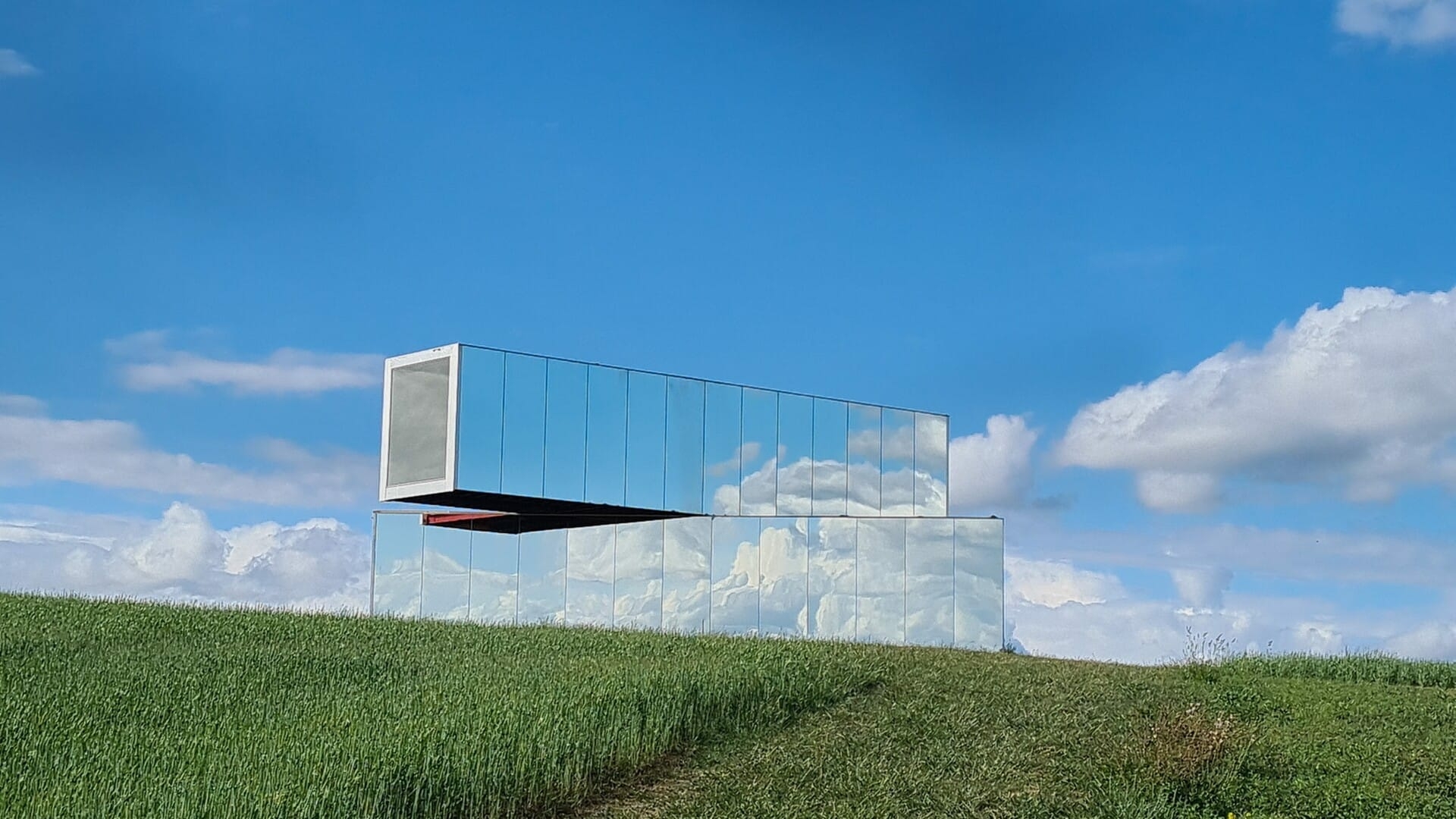 Auf einem Feld wurden verspiegelte Container verdreht übereinander gestellt.