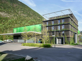 Die Unternehmenszentrale in Südtirol ist ein fünfgeschossiger Kubus in Holzbauweise, die Dachterrasse als Ausnehmung richtet sich nach Süden. Der dunkle Neubau mit Grünfassade rückt dicht an die bestehende Betriebshalle heran.