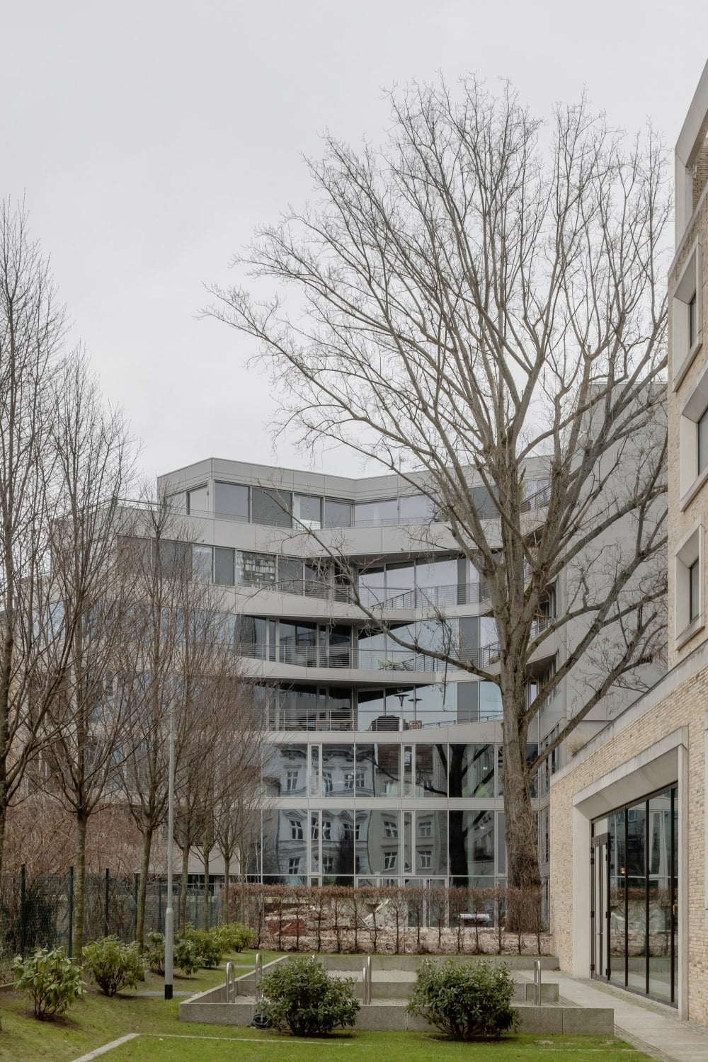 Das Gebäude nutzt die Form des Grundstücks geschickt aus; rückseitig öffnet sich der Bau zu einem großzügigen Grünraum.