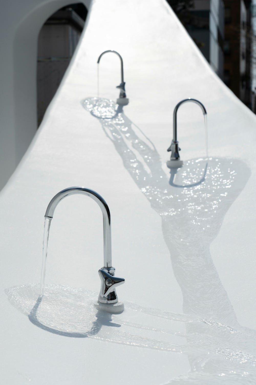 Architekt Sou Fujimoto hat ein weißes, oval geschwungenes Toilettenhaus entworfen, mit Handwaschplätzen und Trinkwasserstellen in unterschiedlichen Höhen.