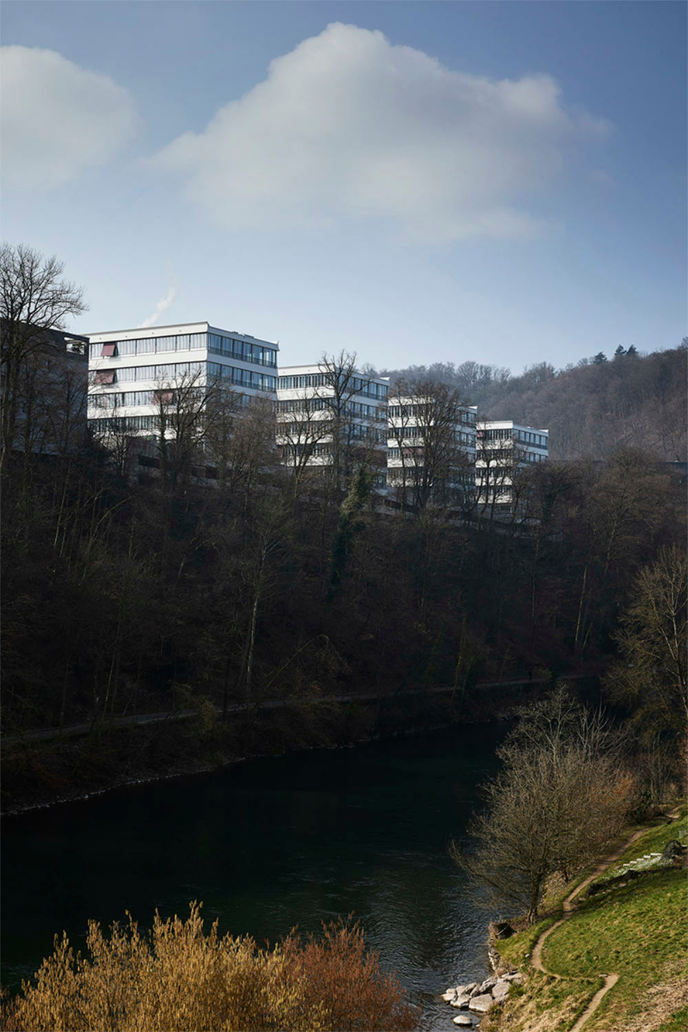 In die vier ehemaligen Gewerbebauten reihen sich entlang eines Steilhangs oberhalb des Flusses Limmat auf.