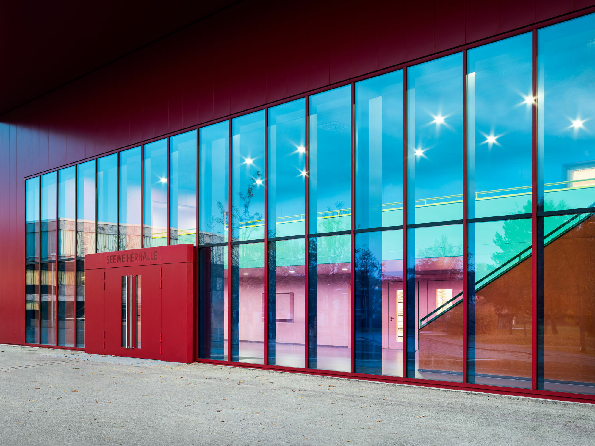 Die Pfosten-Riegel-Fassade ermöglicht einen Blick in das farbenfrohe Innere der Sporthalle.