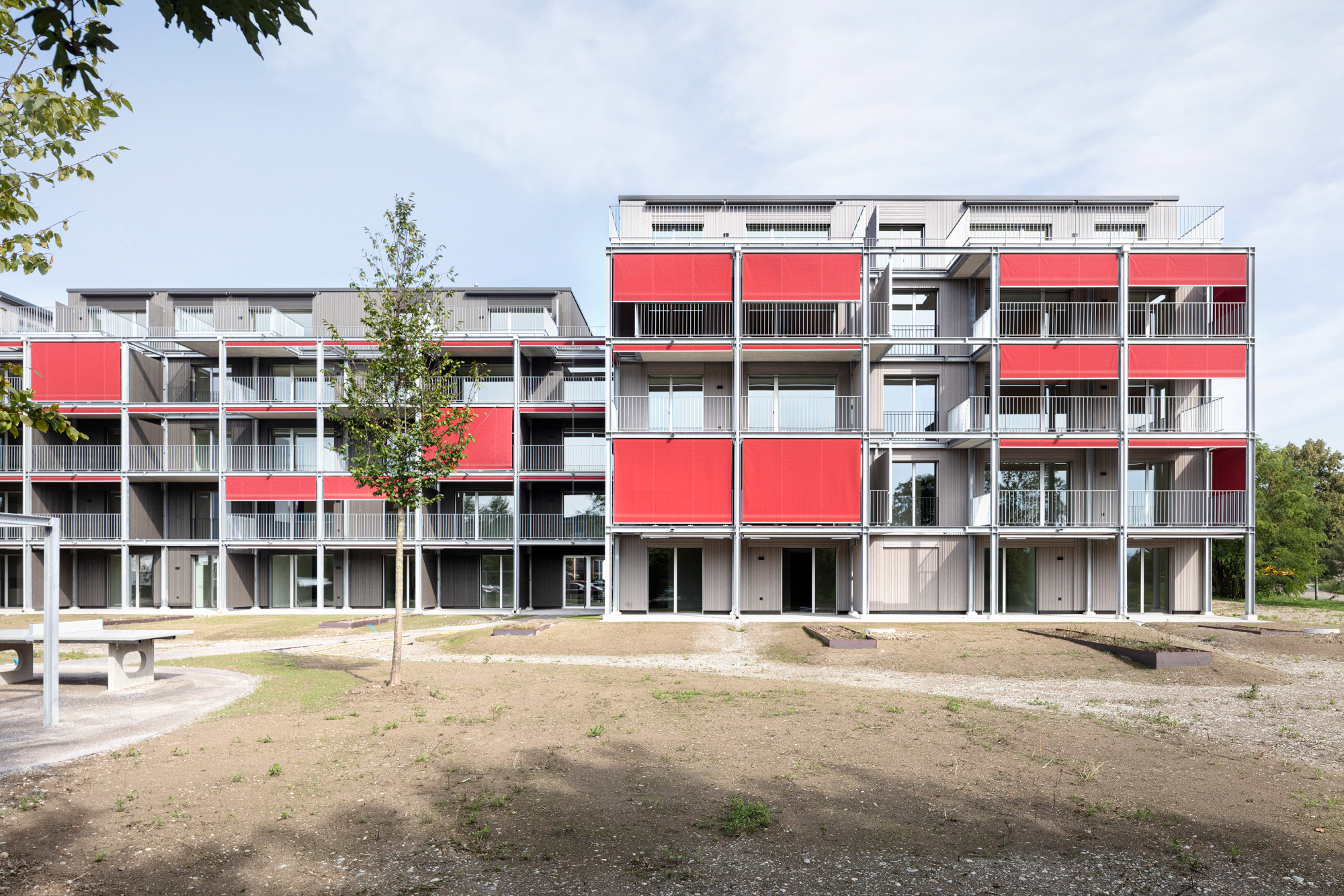 Rote Stoffmarkisen heben sich von den vorvergrauten Holzfassaden ab.