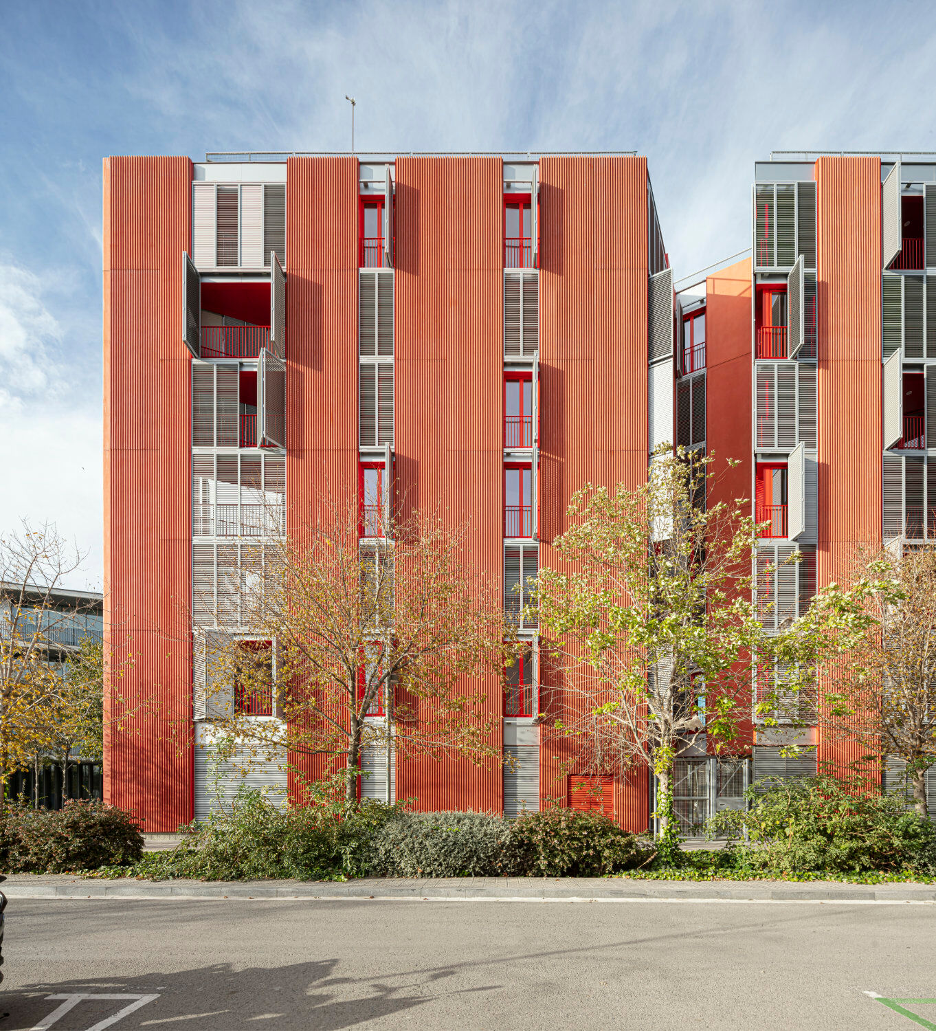 Die Fassaden sind durch vertikale Fensterstreifen und Platten aus geripptem Glasfaserbeton in Rot gegliedert.