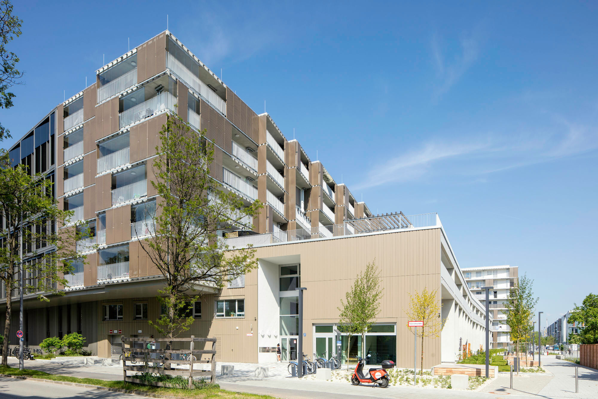 Der neue Quartierbaustein schließt direkt an das benachbarte Bestandsgebäude „Hybrid M“ an, das als L-förmige Mantelbebauung den MVG-Busbetriebshof Moosach auf zwei Seiten umschließt.
