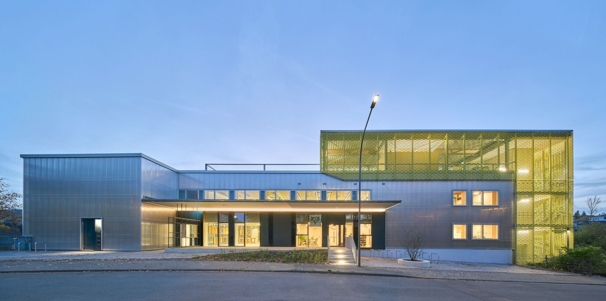 Eine Pfosten-Riegelfassade mit Polycabonat-Stegplatten hüllt die ehemalige Produktionshalle ein.