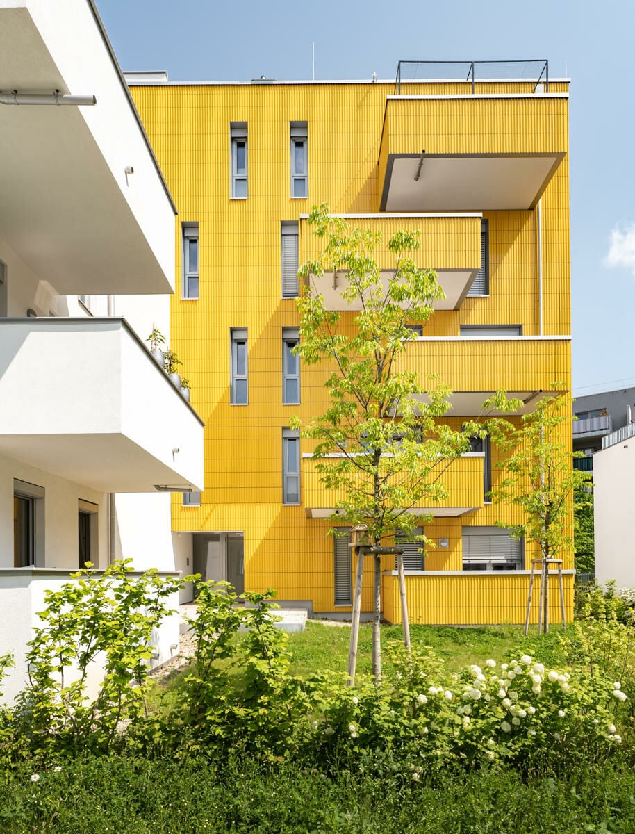 Die keramische Fassade ist profiliert und reflektiert das Sonnenlicht. Die gelbe Farbe hebt die Häuser hervor und inszeniert sie als Teil der gesamten Grünfläche. 