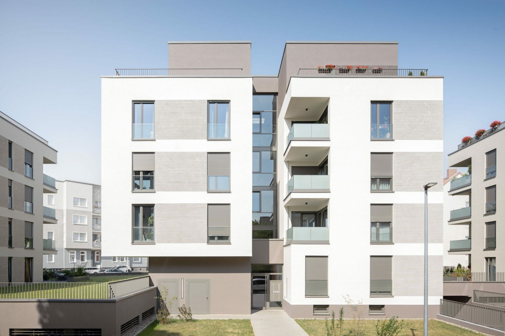 Der Oberflächenwechsel von feinem zum Besenstrichputz, sorgen für eine horizontale Teilung der Fassade. Dadurch soll das Fassadenbild  zum einen gelockert und die Gesamtansicht gestaucht werden.