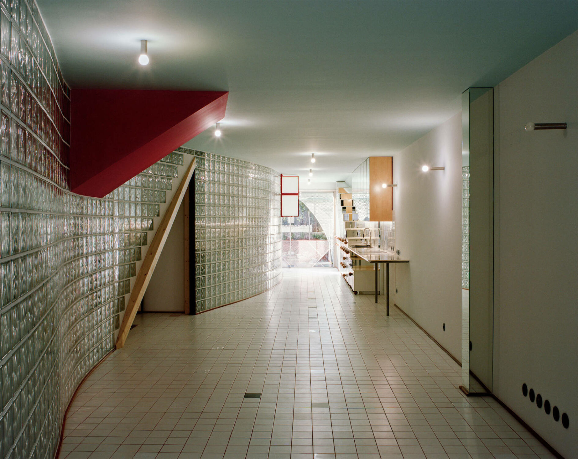 Im Innenraum teilt eine sanft geschwungene Glasbausteinwand den länglichen, rechteckigen Grundriss und schafft eine klare Trennung zwischen gemeinschaftlichen und privaten Bereichen. 