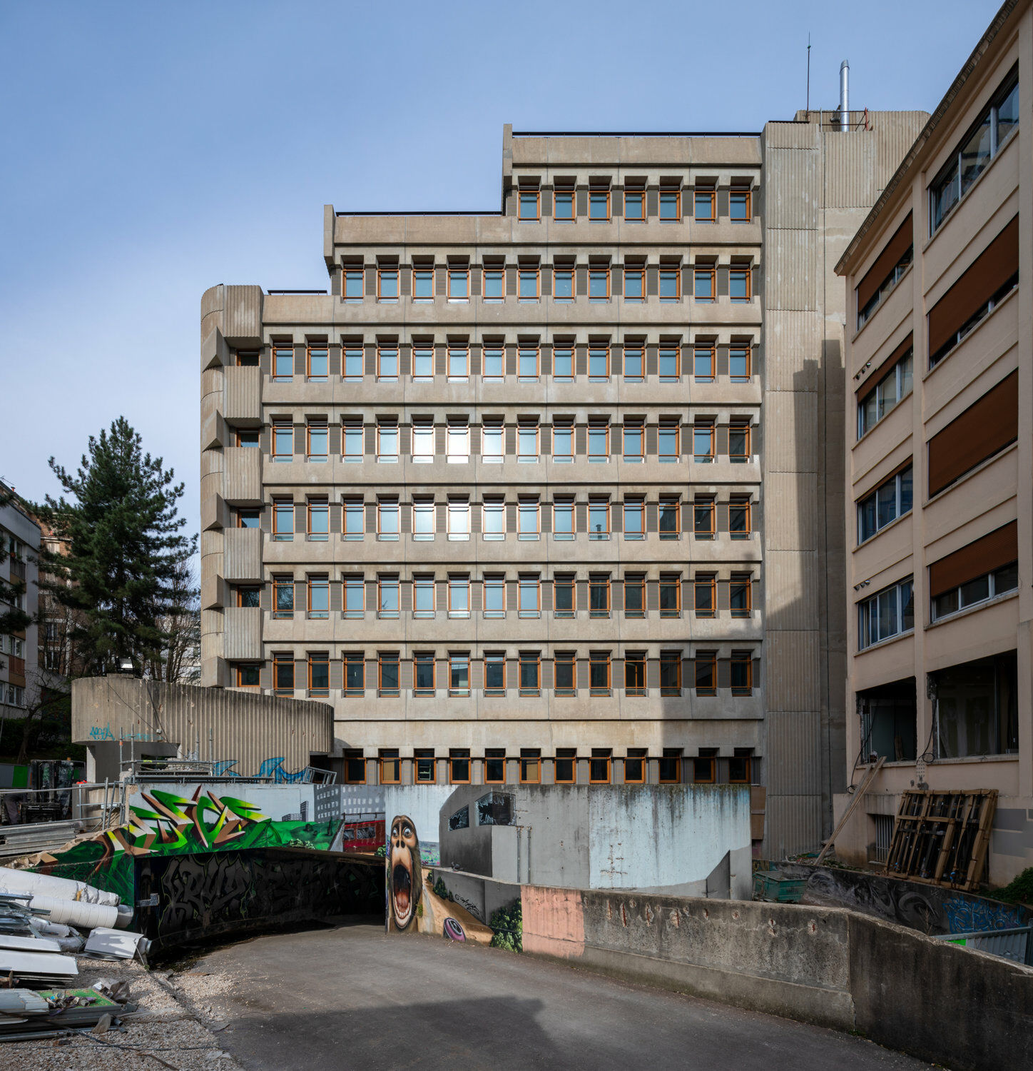 Zwischen dem Siebzigerjahrebau und dem Nachbarhaus schwingen sich die Bahnen einer Doppelhelix-Rampe unter das Hochparterre zur Tiefgarage. 