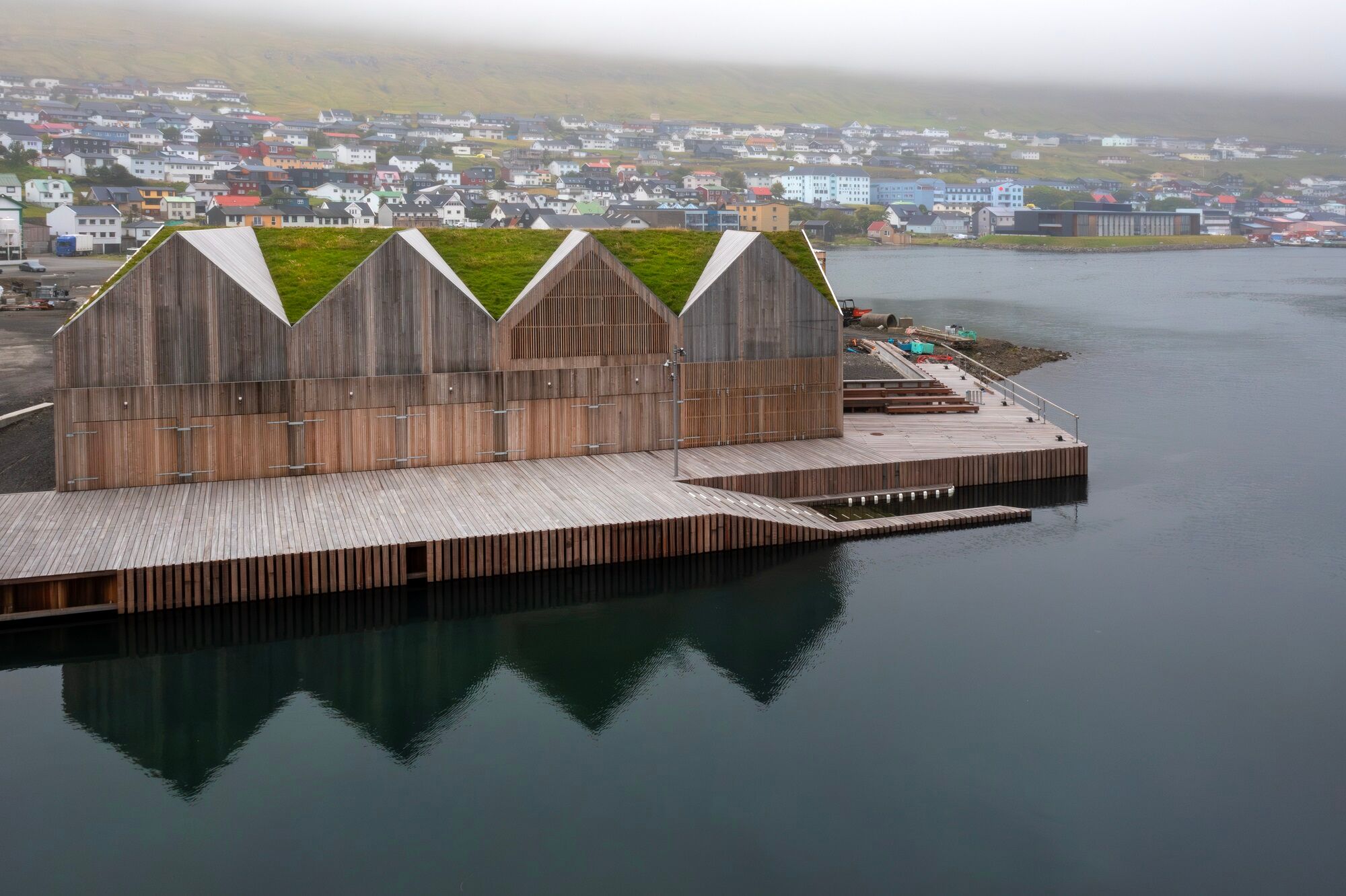 Inspiriert durch die traditionelle Architektur der Färöer Inseln entwarfen die Architekten ein funktionales, langgestrecktes Gebäude mit umlaufender Holzfassade, dreieckigen Giebeln und begrünter Dachlandschaft.