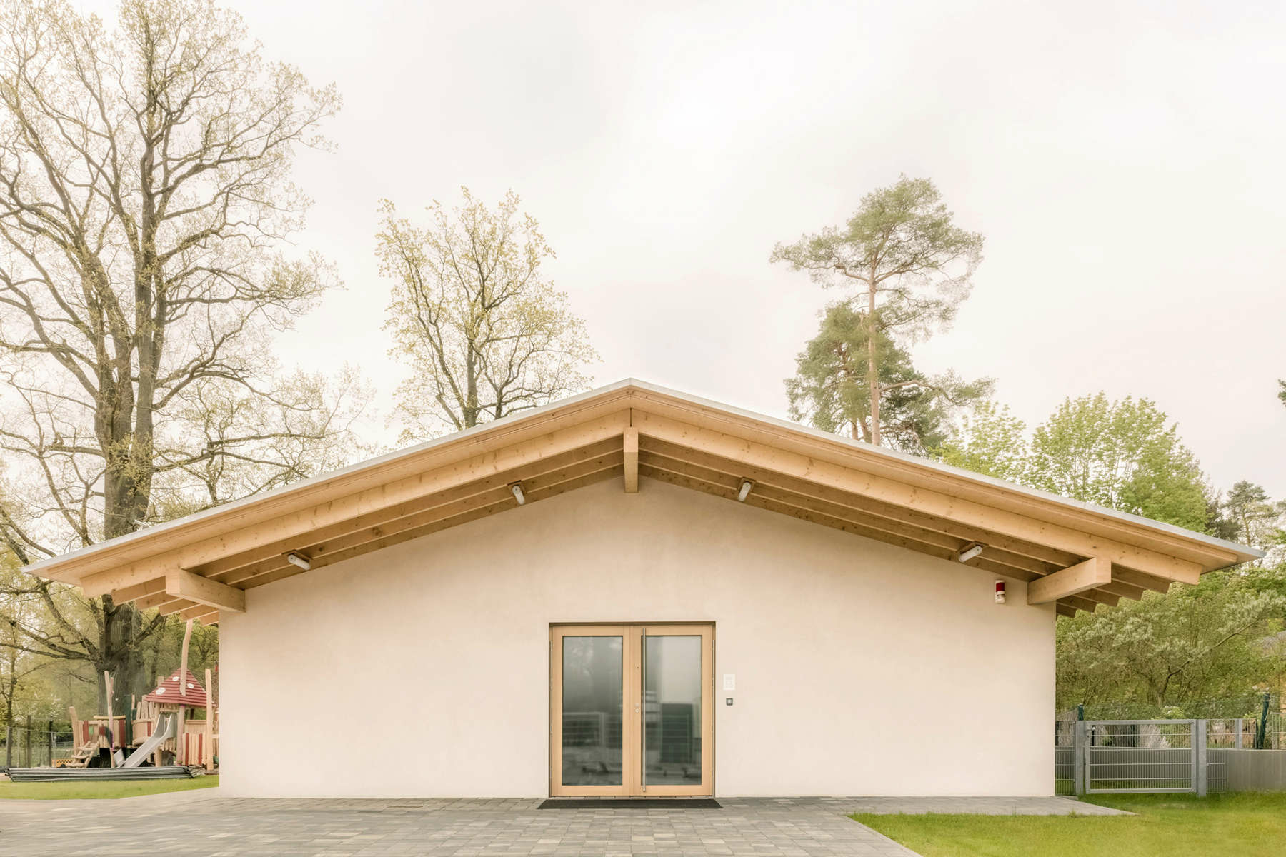 Mit einer natürlichen Material- und Farbwahl und dem flach geneigtem Satteldach mit großen Überständen fügt sich der lange, eingeschossige Neubau behutsam in die dörfliche Idylle ein. 