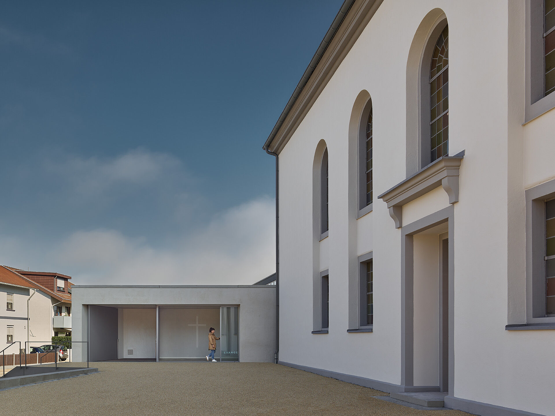 Während sich der eingeschossige Bau zur Straße hin introvertiert zeigt, stellt er mit großer Fensterfront einen eindeutigen Bezug zum gemeinsamen Kirchplatz des Ensembles her.