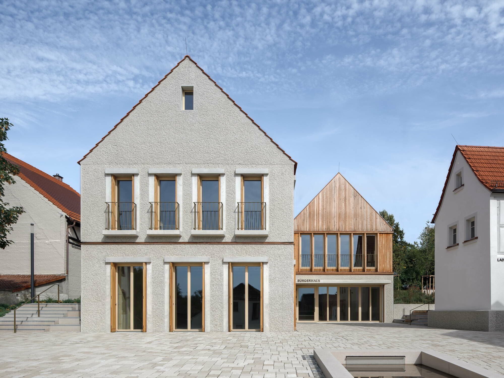 Im Herzen der unterfränkischen Gemeinde Niederwerrn ist am Übergang des Altorts zum gewachsenen Siedlungsgebiet im Sommer 2024 die neue Ortsmitte mit Bürgersaal, Vereinsraum und Café sowie einem Museum und der sogenannten Energiescheune entstanden.