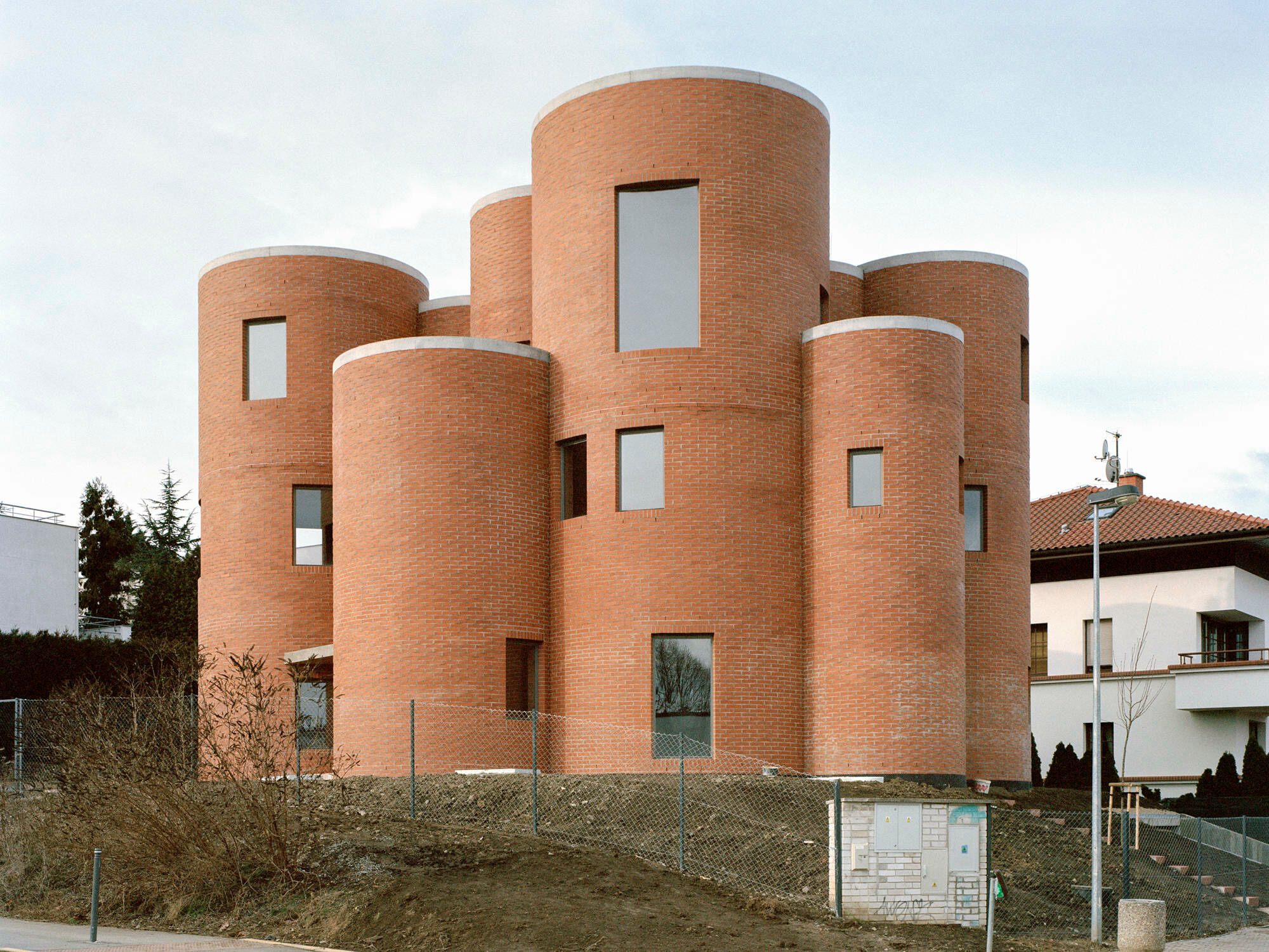 Das unkonventionelle Mehrfamilienhaus in Prag 6 liegt in einer verkehrsberuhigten Spielstraße in einer gutbügerlichen Umgebung mit einigen Villen und viel Grün drumherum.