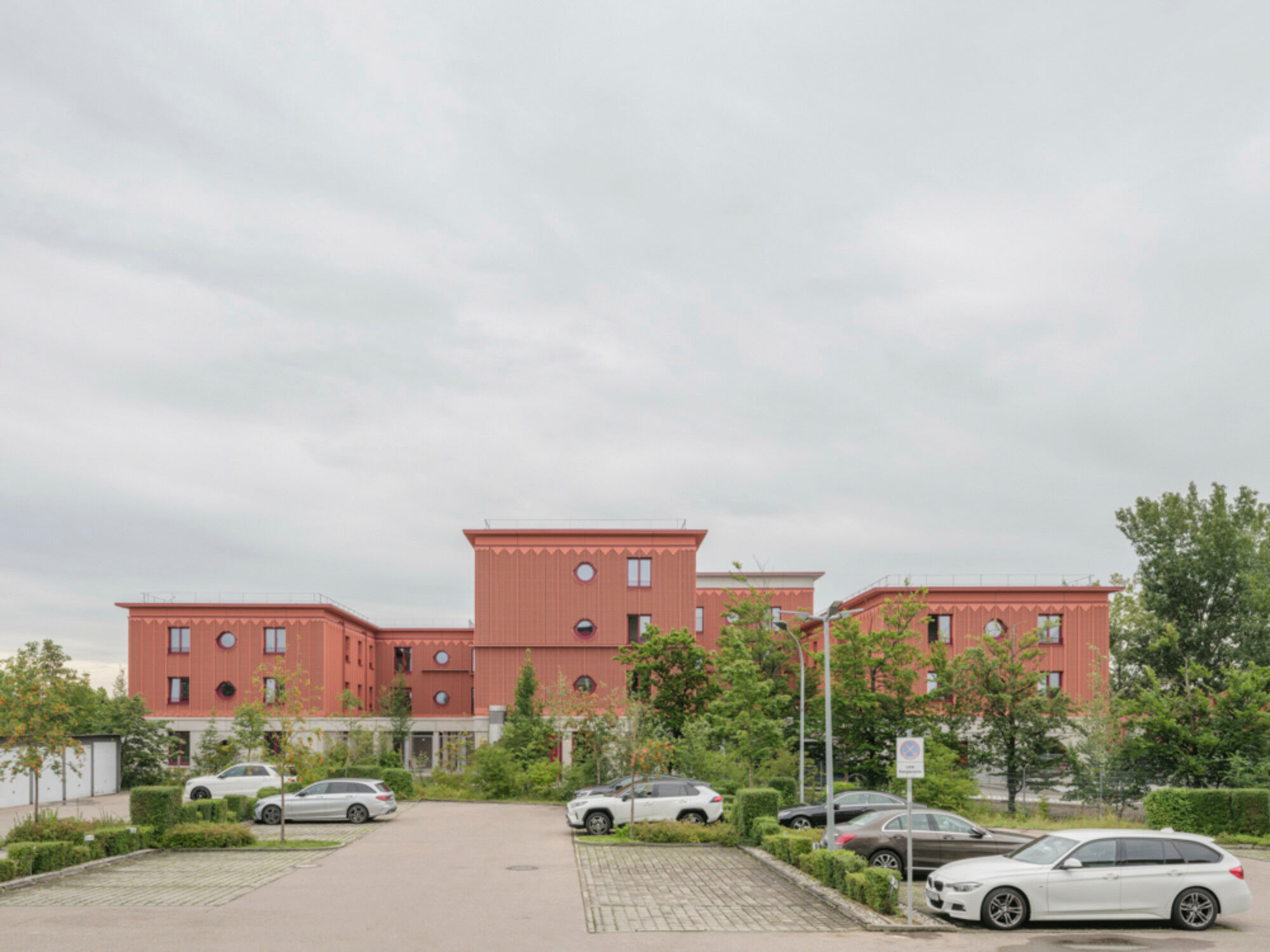 Das warme Rot der Holzfassade, Bordüren unterhalb der Attika und verschiedene Fensterformate sorgen für eine freundlich-lebhafte Wirkung trotz industrieller Vorfertigung der Elemente.