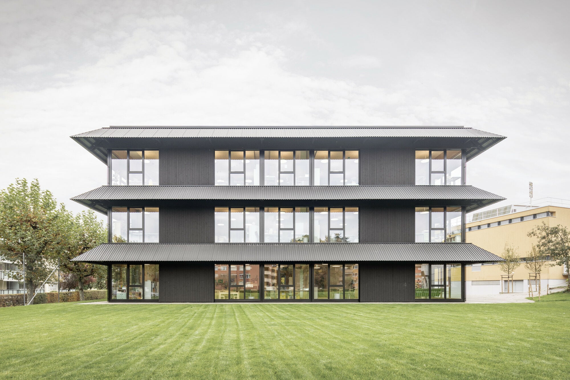 Es handelt sich um einen Hybridskelettbau aus Beton und Holz mit einer Fassade aus Holz, Glas und Metall. Die dunkle Farbe fasst alles in einen gestalterischen Rahmen.