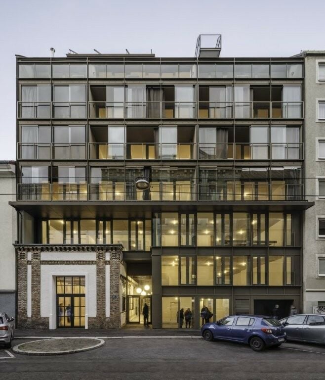 Blickfang ist die zur Straußengasse orientierte, industriell anmutende Glasfassade, die einen Bestandsbau als Spolie in die Gebäudehülle integriert.