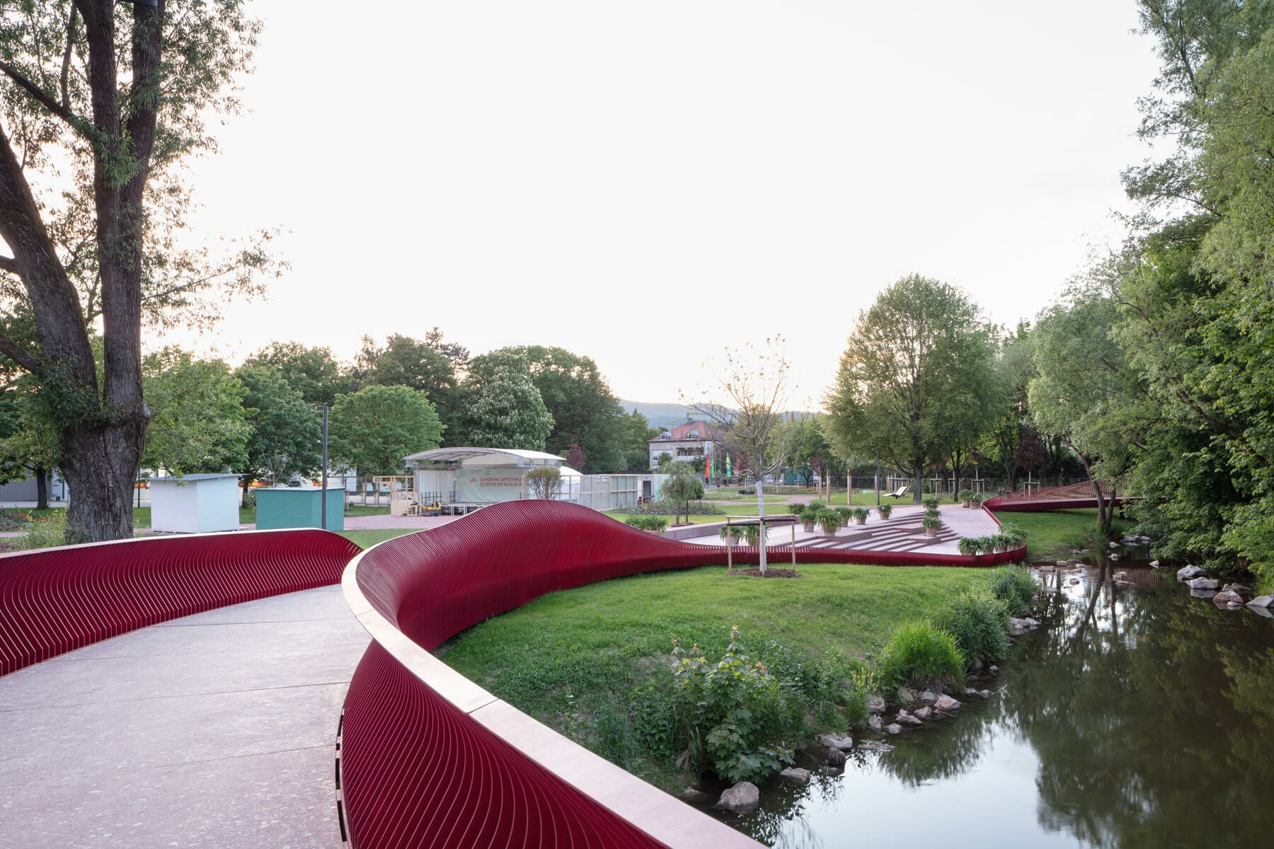 Belegt ist der Steg mit rot eingefärbten Betonplatten, die mit regionalem Flusskiesel in Terrazzo-Optik gestaltet sind. 