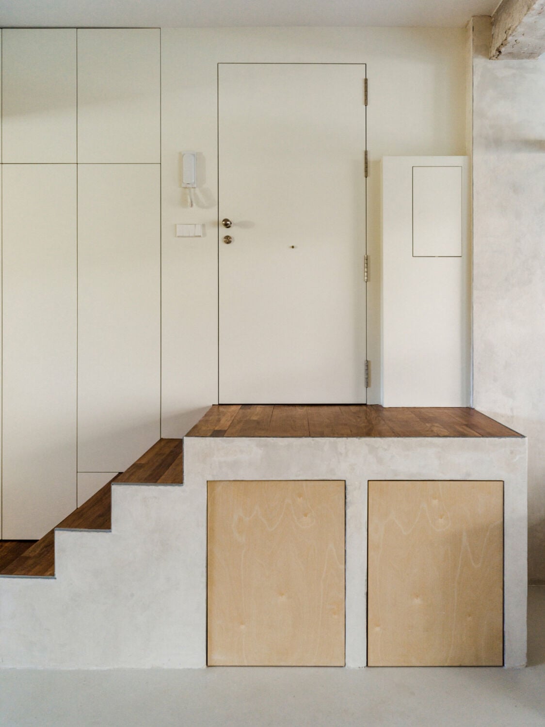 Von einem massiven Podest, das als Stauraum dient, führt eine fünfstufige Treppe hinab in den Wohnraum.