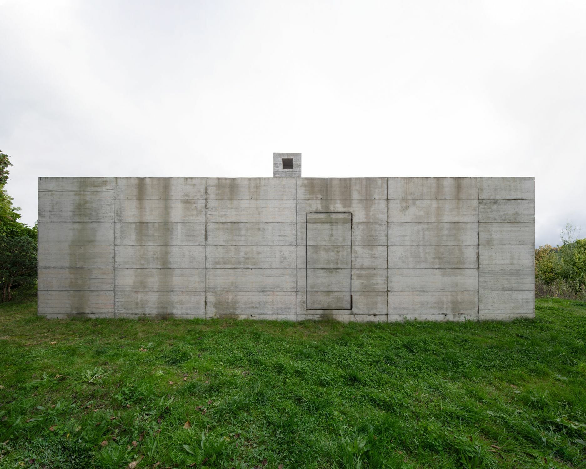 In das regelmäßige Fugenmuster der Sichtbetonfassade nach Westen fügt sich fast unmerkllich eine Betontür ein. 