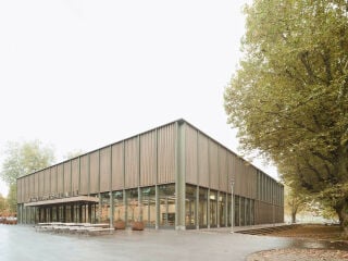 An der Nordseite öffnet sich das Erdgeschoss mit bodentiefen Glasflächen und markiert den Haupteingang mit Foyer und Cafeteria.