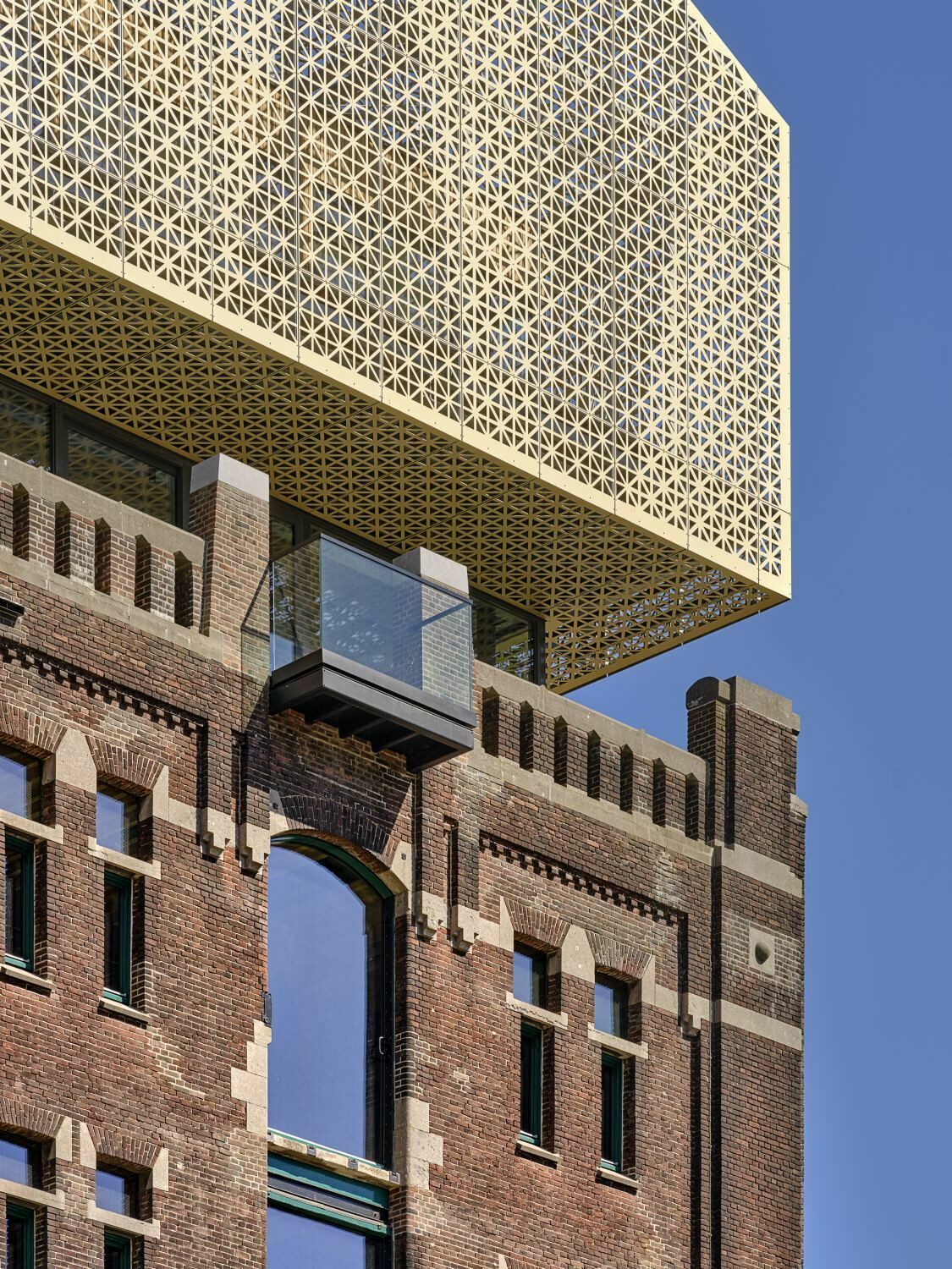 Die goldene Aluminiumfassade verdeckt das oberste Geschoss und die Technikaufbauten auf dem Dach. Aus dem Blech wurden Dreiecke in unterschiedlicher Dichte ausgestanzt.
