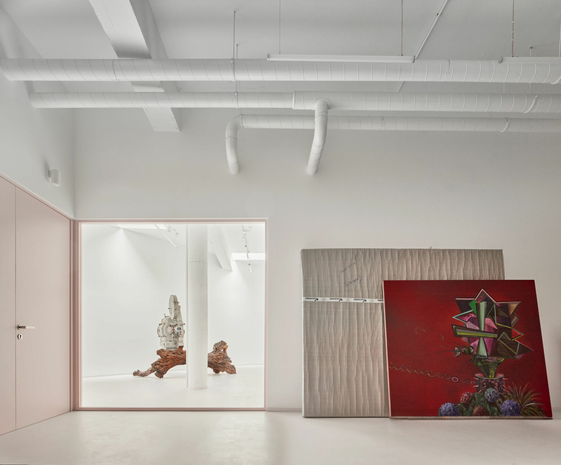Eine großzügige Glaswand mit rosafarbenem Aluminiumrahmen ermöglicht Sichtbezüge zum angrenzenden Ausstellungsraum.