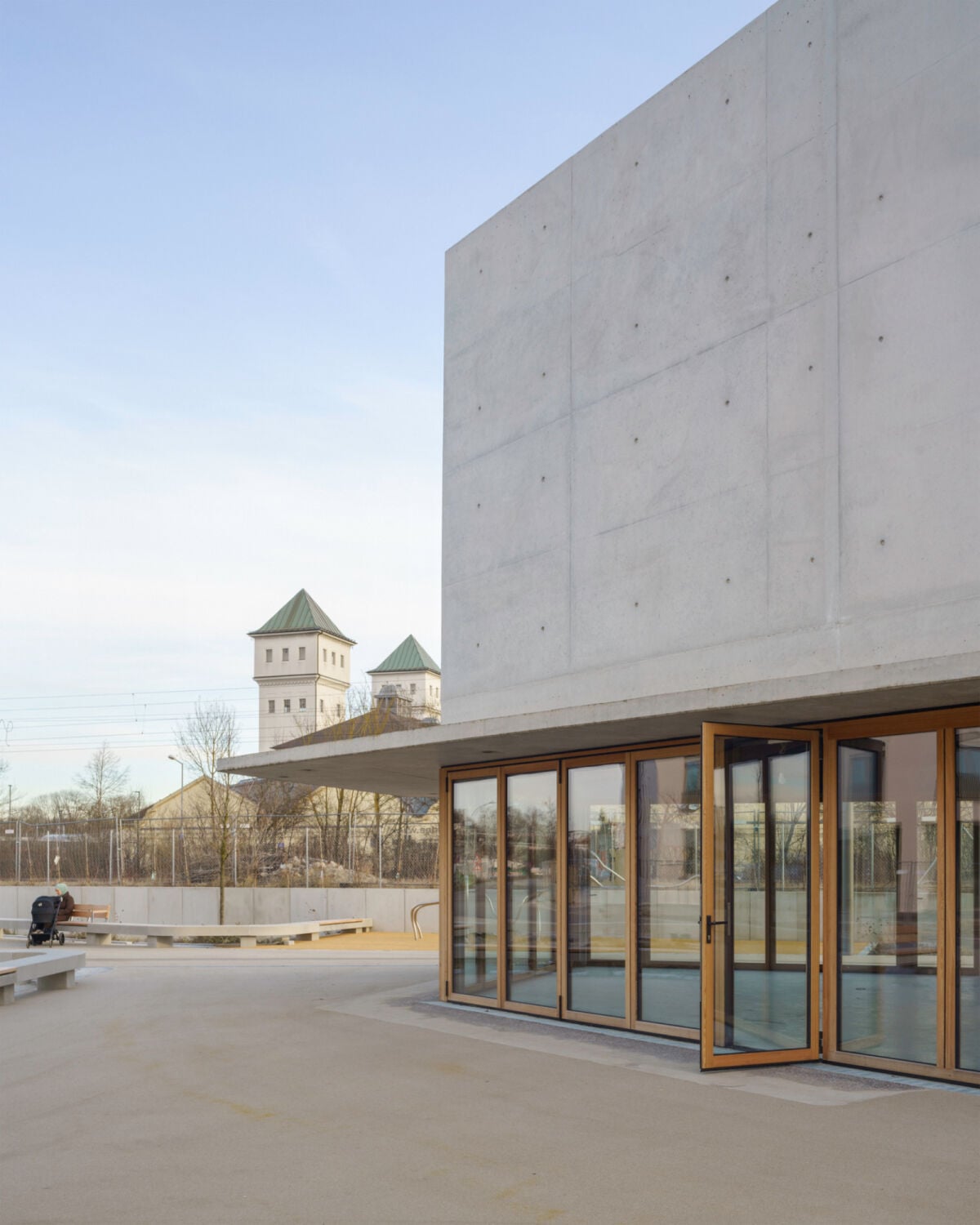Darüber schließt die massive Sichtbetonfassade mit einem schmal auskragenden Gesims ab, das die Holzverkleidung schützt und sich im Bereich der Glas-Faltwände zu einem eleganten Vordach ausweitet.