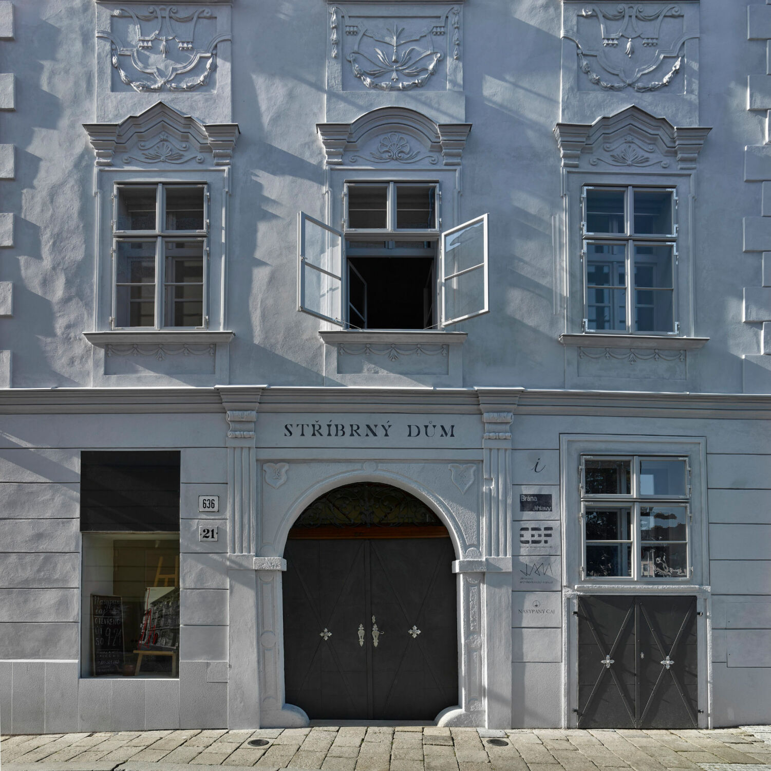 Traditionelle, doppelflügelige Holzkastenfenster, die durch einen Mittelpfosten, Sprossen und einen Kämpfer gegliedert sind und dekorativer Feston prägen die hellgrau gestrichene Fassade. 