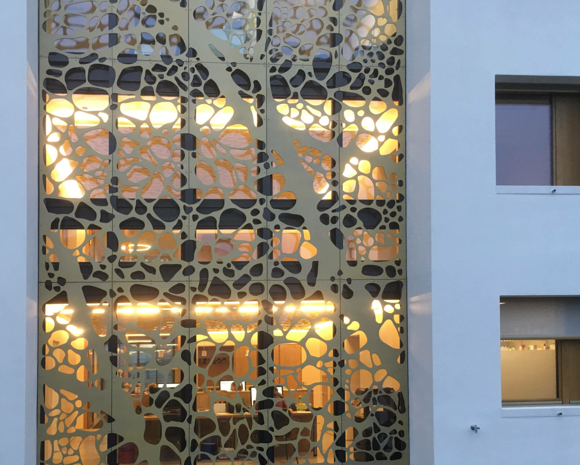 Eingangsbereich mit markanter Goldfassade: Die perforierten Paneele verbinden Sonnenschutz, Belichtung und Orientierung.