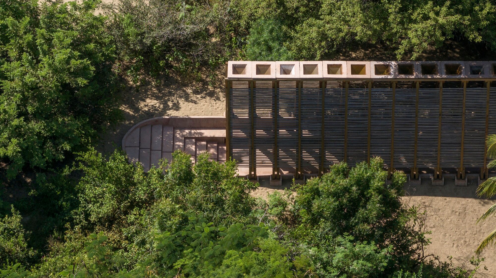 Die offene Lamellenstruktur ist licht- und luftdurchlässig, den First bilden umgekehrt pyramidenförmige (also trichterförmige) Wasserbecken.