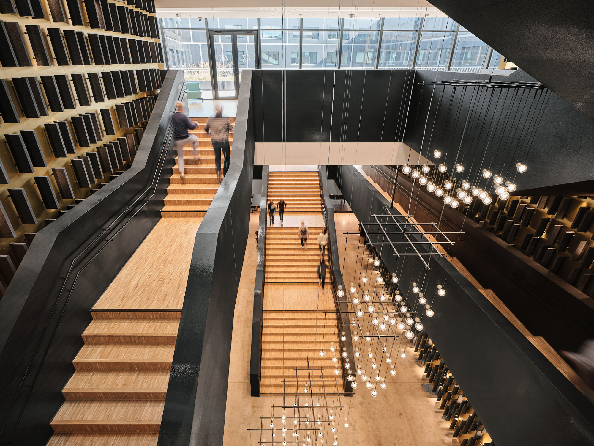 Der Haupteingang führt ins gebäudehohe Foyer mit breiten Treppen und festlichen Leuchten. 
