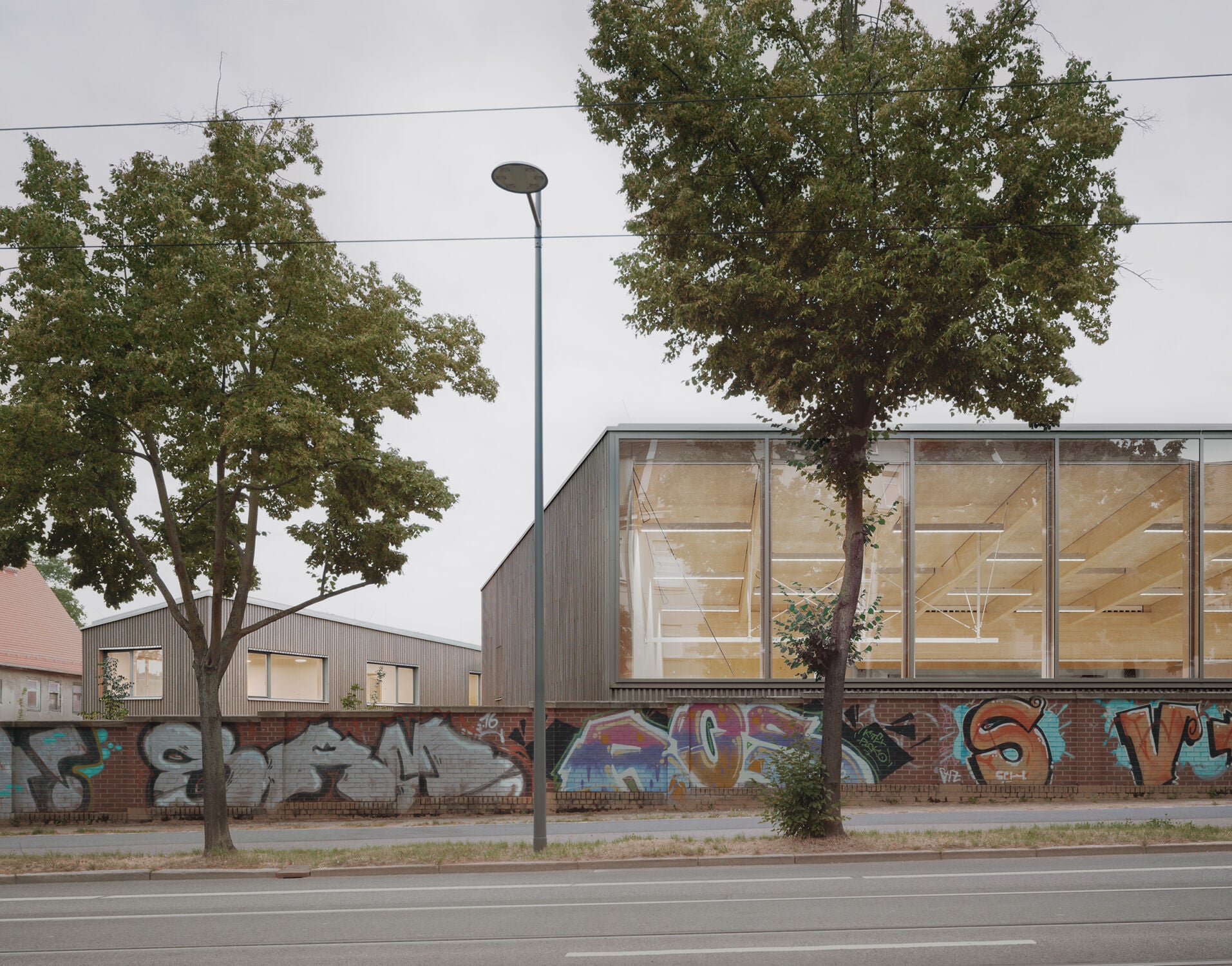 Eine denkmalgeschützte Backsteinmauer begrenzt das Schulgelände im Osten; dahinter erhebt sich die Glasfassade der Mehrzweckhalle.