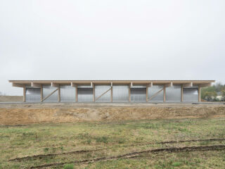 Die schlichte Halle hat ein Holztragwerk, eine Fassade aus Polycarbonat und eine Dachdeckung aus Metall.