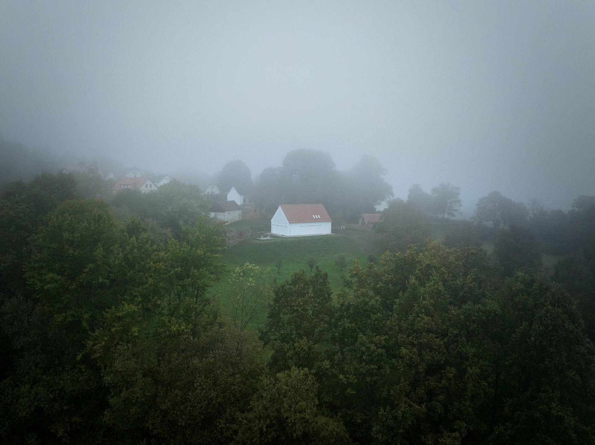 Der Neubau liegt auf einer Anhöhe, umgeben von Bäumen, einem Teich und einer Mauer.