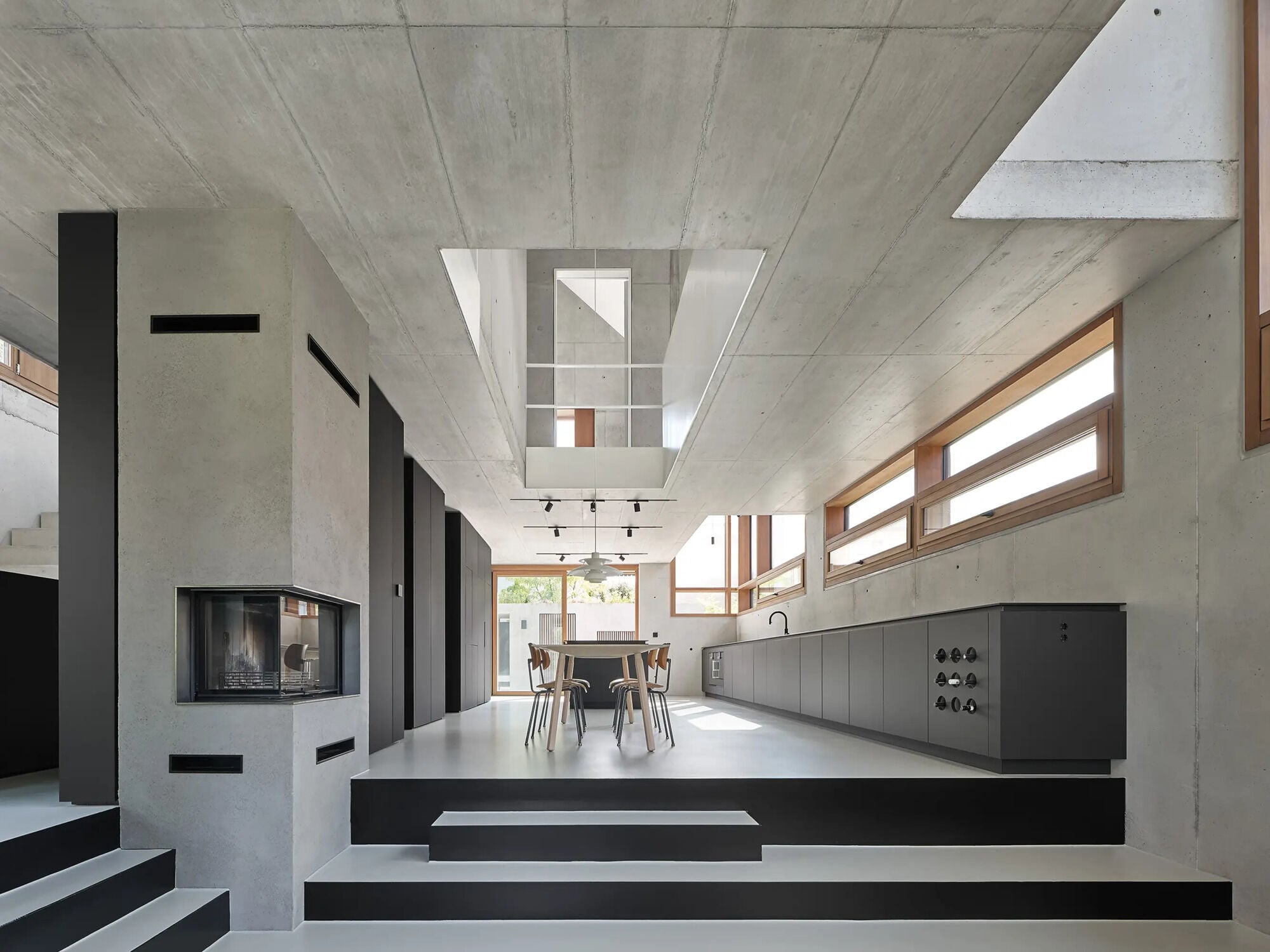 Das Haus JES in Winnenden, entworfen von Rommel, Wagenpfeil Architekten: Zur Straße fasst eine helle Sichtbetonwand den Hof, darüber hebt sich das schwarz verkleidete Langhaus aus der Bepflanzung.