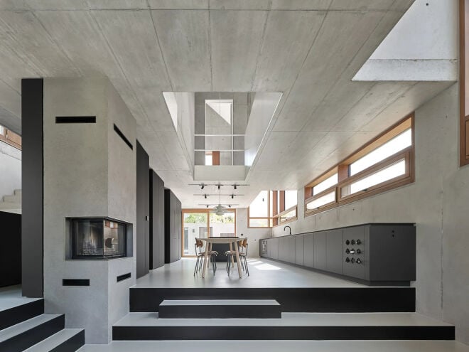 Das Haus JES in Winnenden, entworfen von Rommel, Wagenpfeil Architekten: Zur Straße fasst eine helle Sichtbetonwand den Hof, darüber hebt sich das schwarz verkleidete Langhaus aus der Bepflanzung.