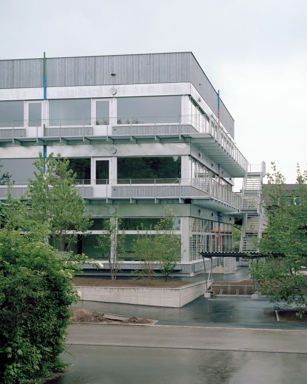 Außen wechseln sich Bänder aus einer vorvergrauten Fichtenholzlattung, großzügige Fenster, helle Geschossgrenzen und Profile sowie vorgesetzte, filigrane Fluchtbalkone und -treppen aus Metall ab.