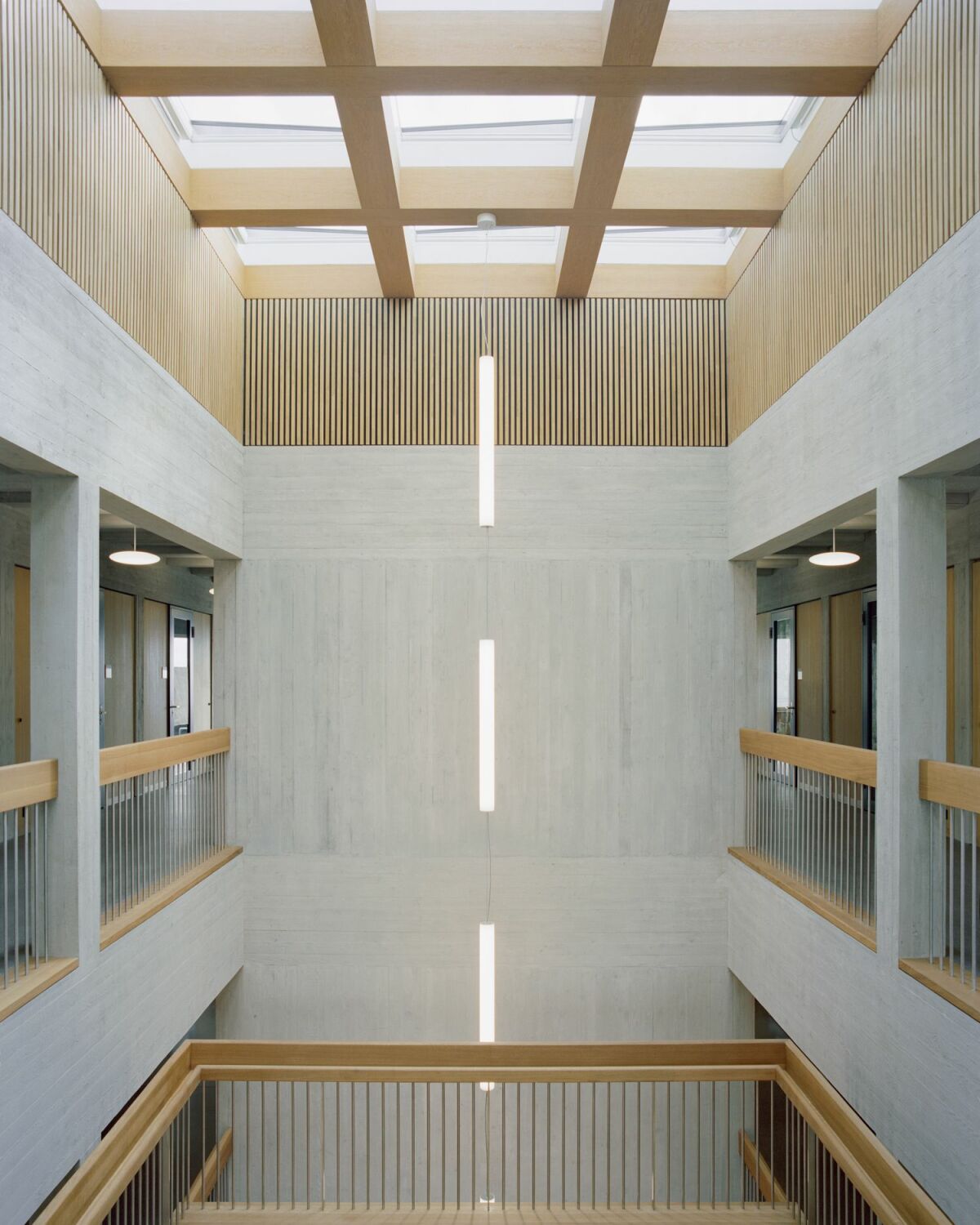 Die zentrale Erschließungsachse weist zahlreiche Details auf: Der fein strukturierte Sichtbeton wechselt sich mit konstruktiven und verkleidenden Holzelementen ab, oberer Lichteinfall in das Atrium, Sichtbezüge in die flankierenden Klassenebenen und eine offene Treppenanlage ergänzen das Konzept.