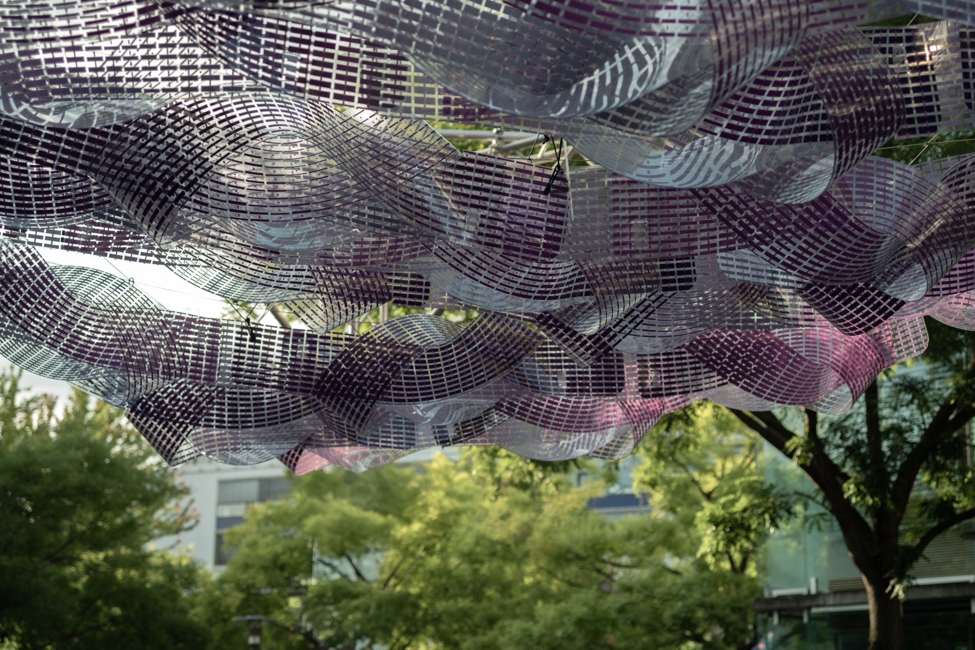 In einem filigranen Seilnetz hängen die aus Polycarbonatbändern geformten „Loops“, die als Trägerstruktur für organisch gebogenen Photovoltaik-Module dienen.