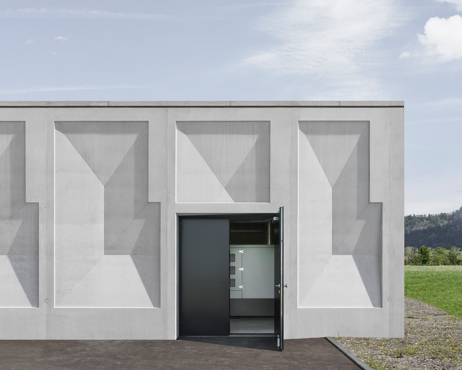 Farbakzente des Sichtbeton-Neubaus sind zwei große, in tiefem dunkelblau lackierte Metalltore.
