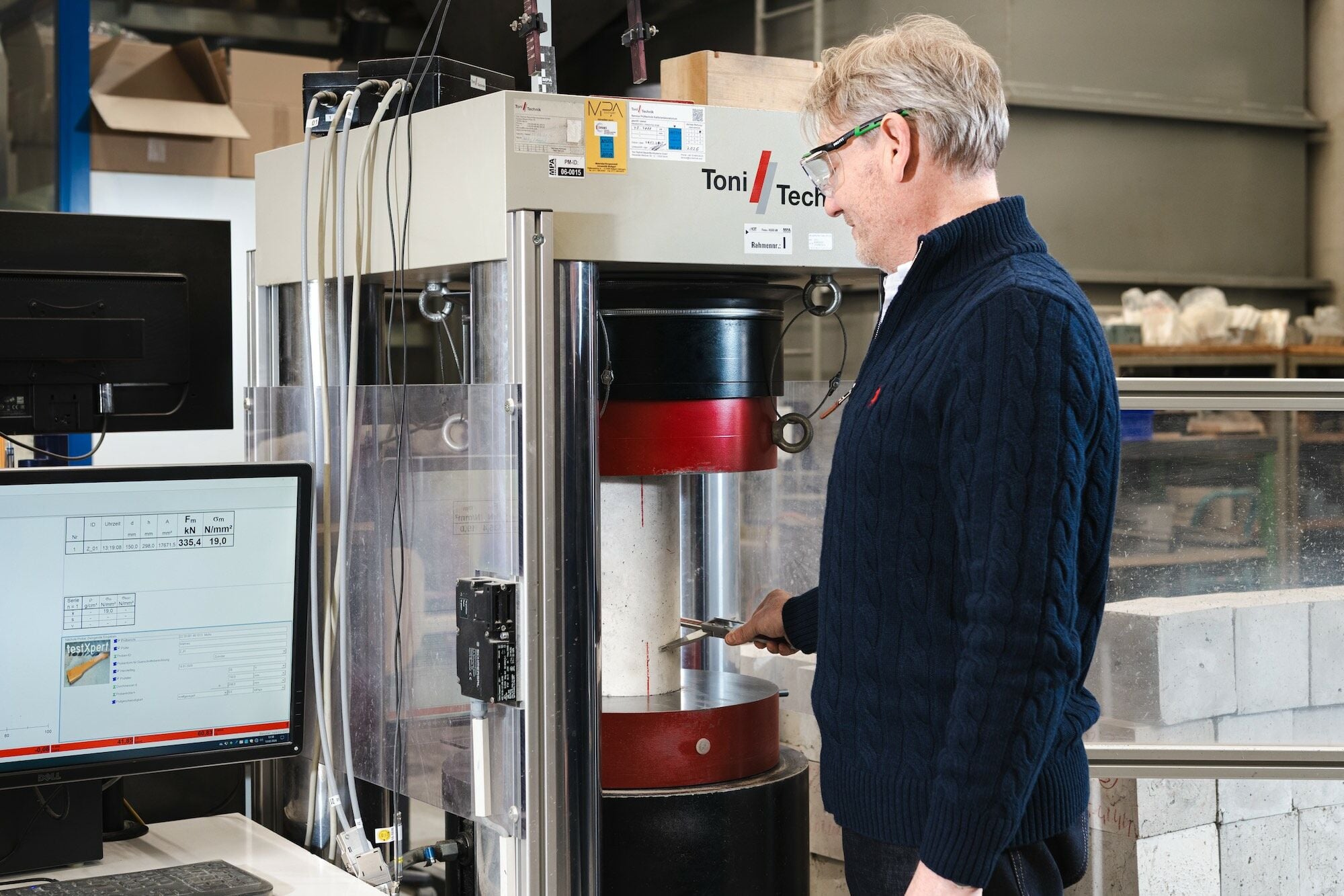 Professor Frank Dehn begutachtet einen zylindrischen Betonprüfkörper während der Druckprüfung. Die Versuche liefern Kennwerte zur Festigkeit und zum Verhalten des Materials unter Belastung.