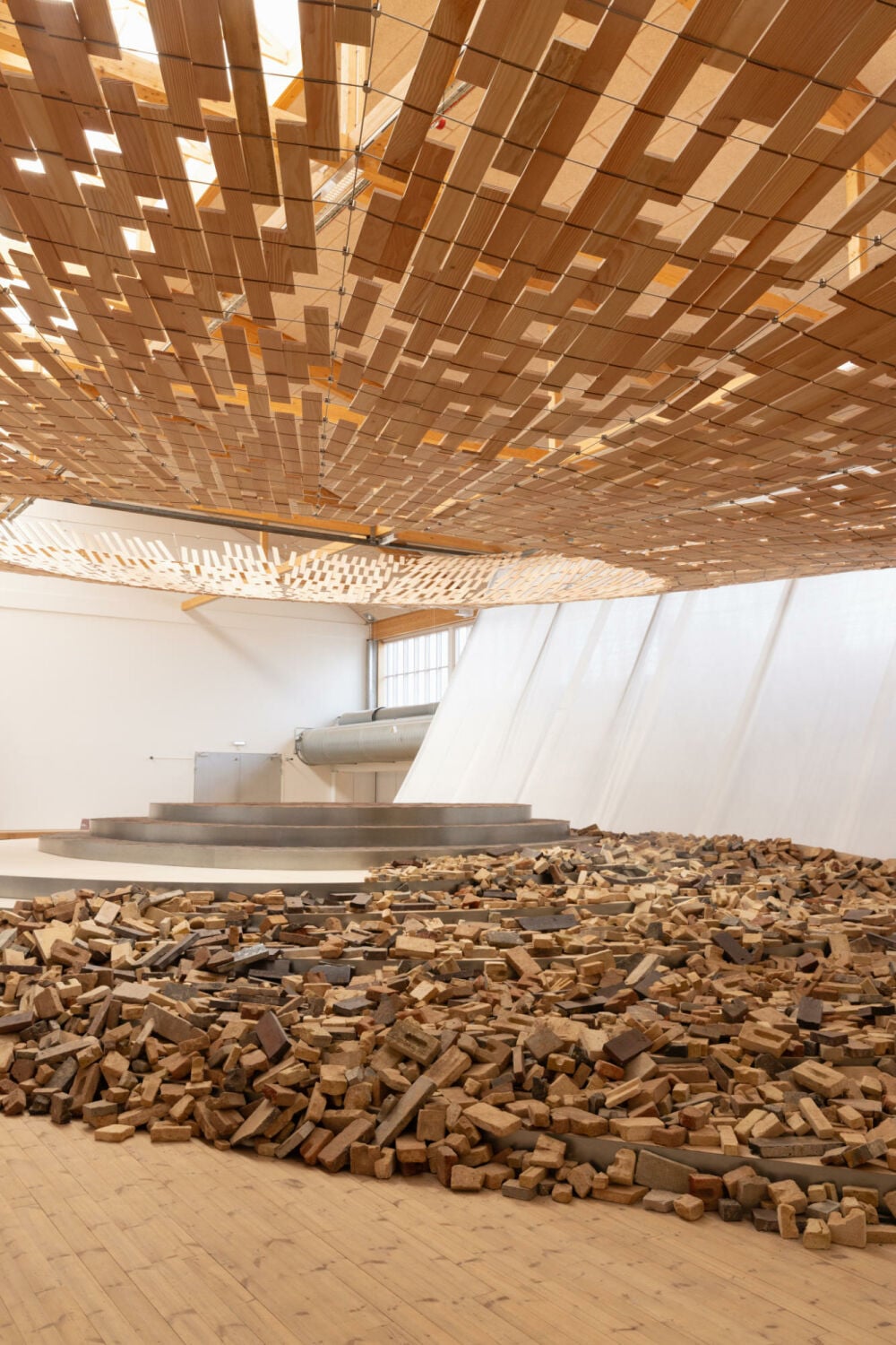 Locker verteilte Holzstücke und Ziegelsteine umgeben die Podeste und gehen zum Rand hin allmählich in eine sandige Fläche über.