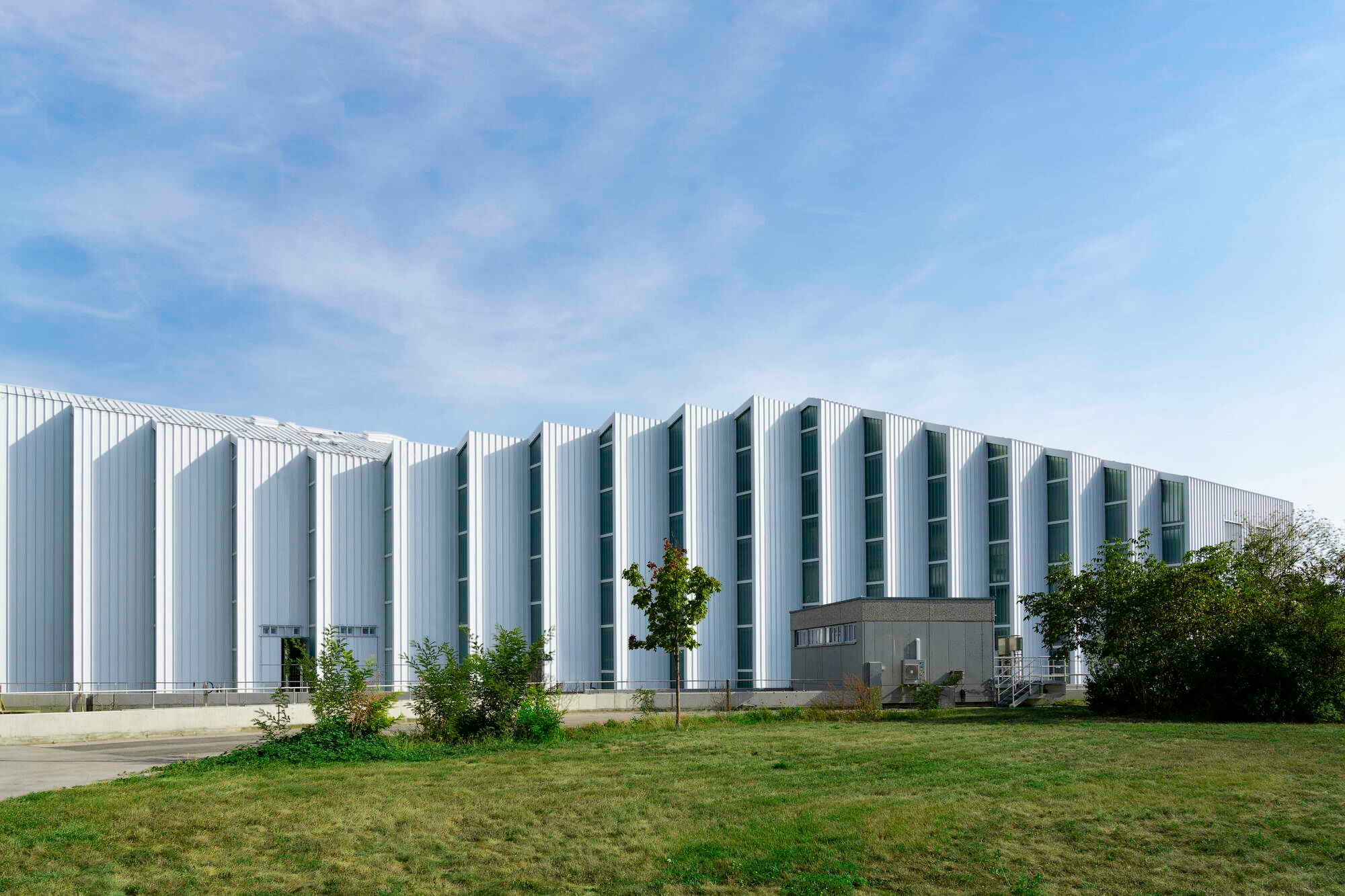 Zur Nordseite ist die Fassade aus weißem, profiliertem Aluminiumblech aufgefächert.