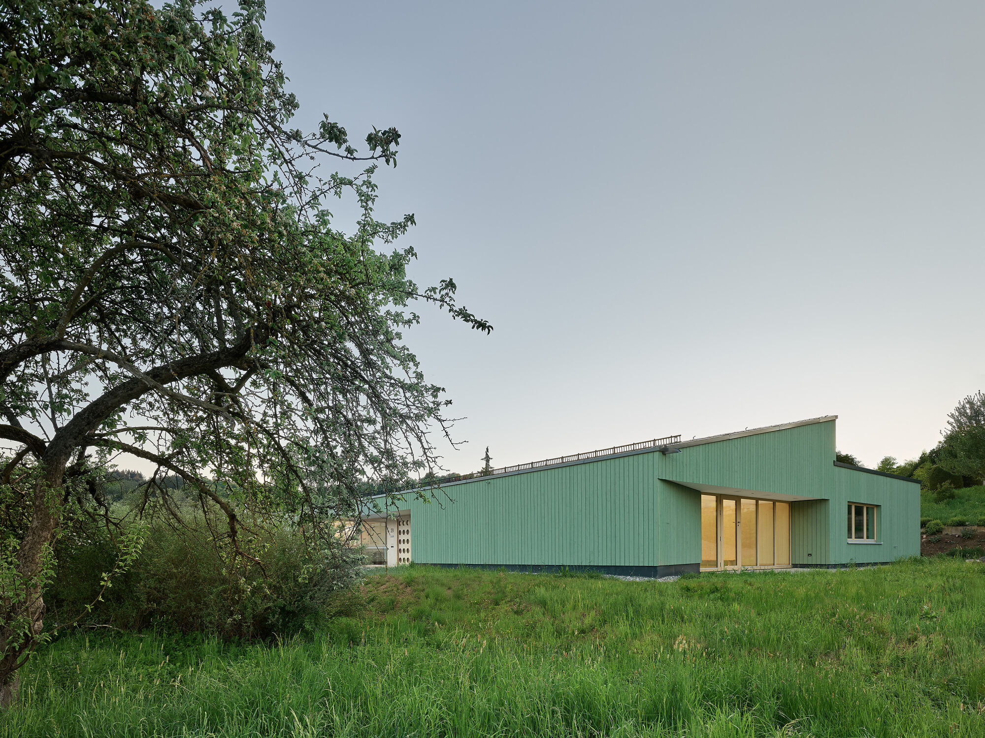 Mit seiner markanten, grün lasierten Holzfassade fügt sich das Gebäude harmonisch in die Landschaft ein.
